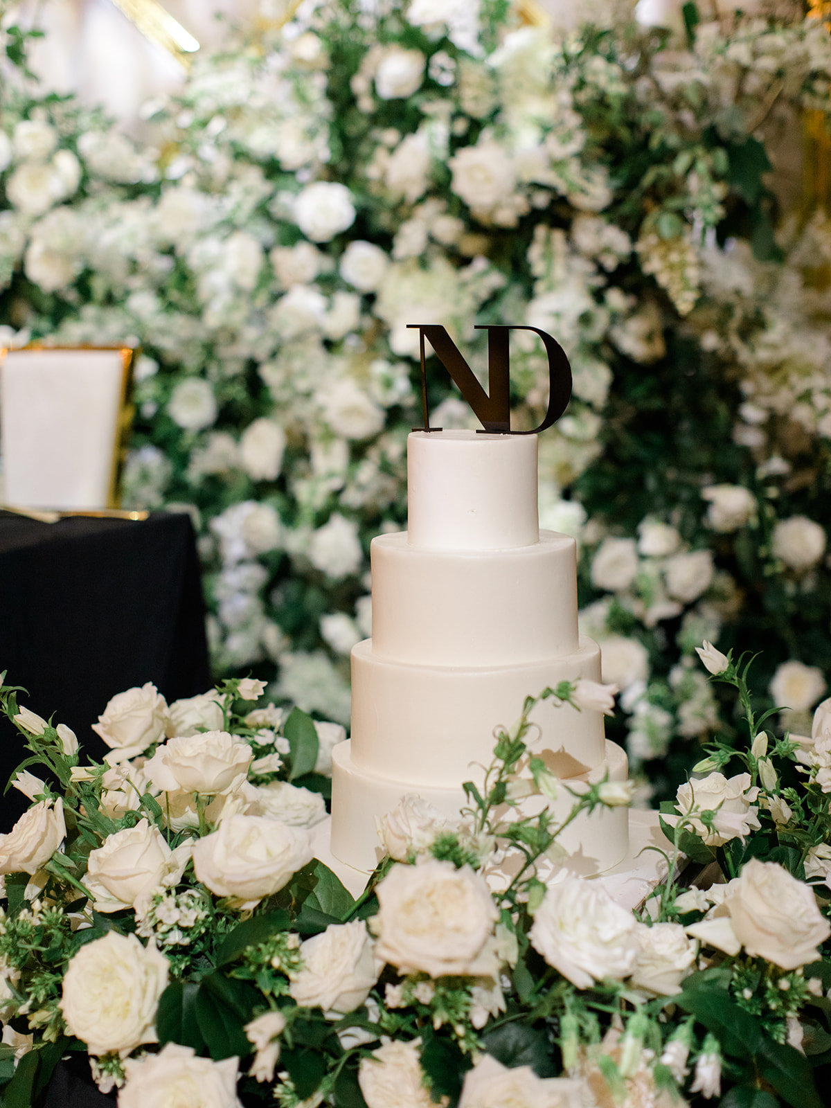 A white tiered cake surrounded by white roses