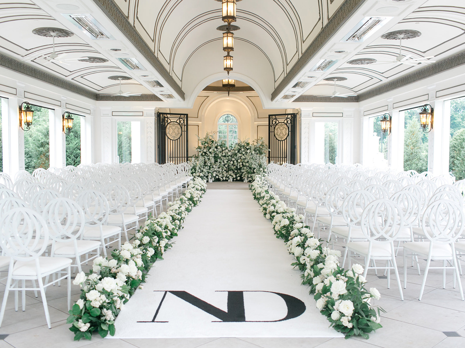 A white ceremony aisle lined with roses beneath a vaulted ceiling
