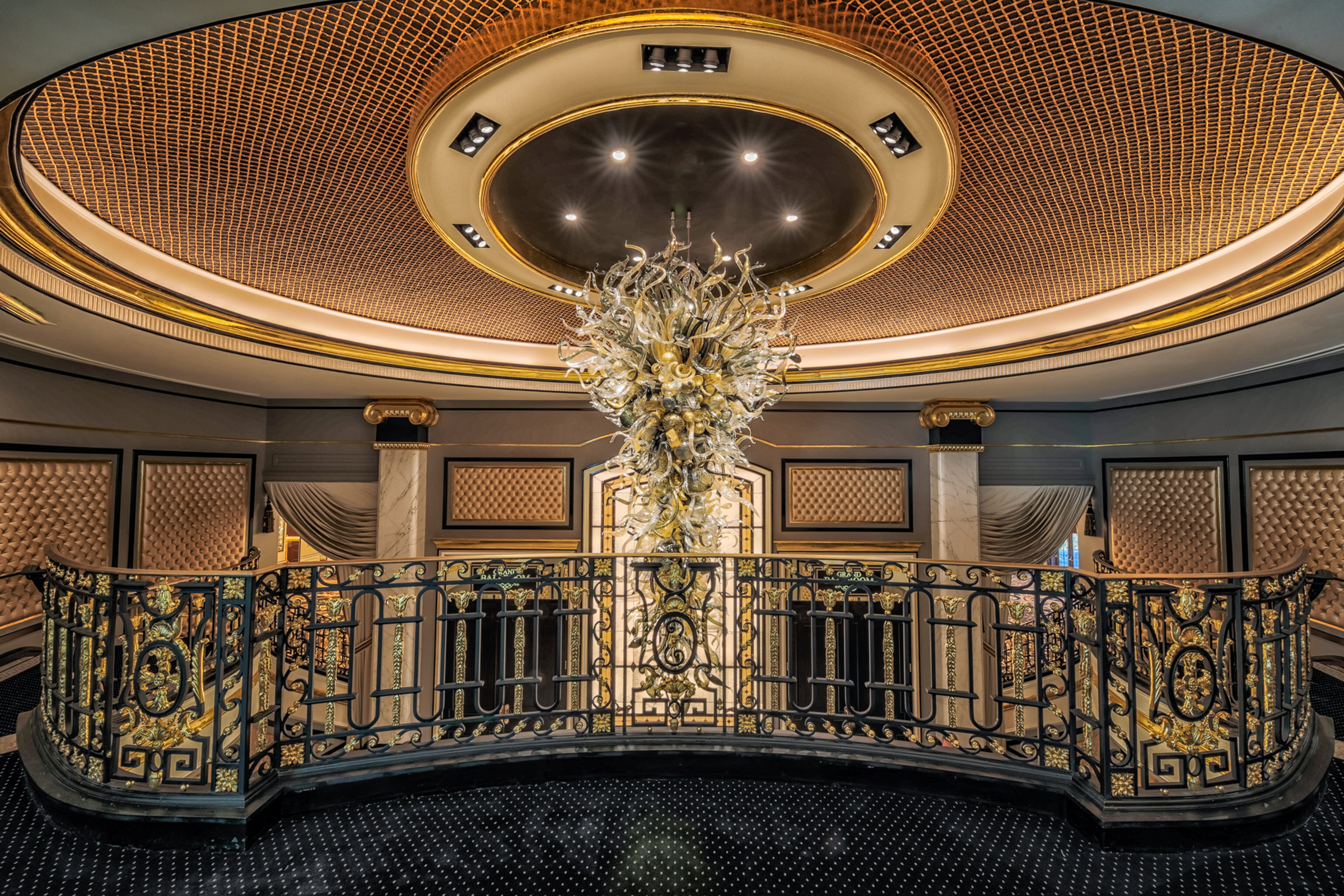 A golden chandelier above the gilded rotunda balcony